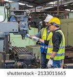 Male Factory engineer and male worker in safety work uniform (hard helmet and vest) are checking heavy machinery in an industrial manufacturing factory, Factory workers concentrate with heavy machine