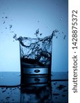 Small photo of Single glass of water ice cube trow droplets splash fresh cold blue light liquid reflection