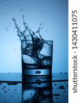 Small photo of Single glass of water two ice cubes trow droplets splash fresh cold blue light liquid reflection