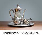 Small photo of Ornate 4-piece tea set on table. Silver or silver plated tea pot, sugar bowl and cream or milk jug. Ornamental silverware to serve hot tea or coffee. Selective focus.
