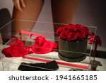 Women's red underwear with roses in showcase through store window. Women's fashion shop display. Beautiful, romatnic arrangement. Blurred background. Selective focus on flowers. Close up, copy space