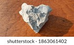 Small photo of A piece of gray hardened cement in the shape of a heart, on a brown wooden table (top view).
