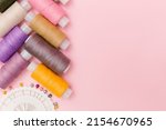 Sewing tools and sewing accessories on elegant pink background. Dressmaking, tailor background. Multicolor sewing threads, thread spools, needles, pins. Top view, flat lay for tailor's business.