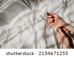 Elegant hands lie on the white bed sheet in the sunlight. Bed with white linens. The concept of a good morning, stress relief, self-care, relaxation and time for yourself