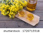 bottle and cups with rapeseed oil, next to young rapeseed flowers on a wooden table