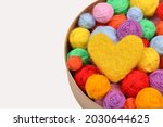 A lot of multi-colored wool balls of yarn with a yellow wool heart in a round cardboard box on a white background.Handmade concept, favorite hobby, thread sales.Rainbow layout of a needlework store.