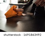 Young woman using orange microfibre cloth and spray bottle to clean/sanitise dark worktop surface