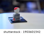 Small photo of Office Stamp with Four Rolling Wheels, Resting on an Open Stamp Pad Filled with Blue Ink. Red Details on the Stamp Head and Body. White, Curved Office Desk. Blurred Background, Window Reflections