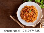 Top view of Instant noodles spicy with chicken, mushroom, white sesame, seaweed sheets and chili in white plate on wooden table background. Asia Food