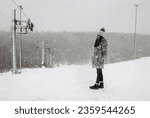 Girl in winter coat standing on slope near loop-line ski drag during snowfall. beautiful winter view in snowy weather. Mountain skiing and snowboarding during heavy snowfall