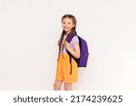 Small photo of A little girl with pigtails and shorts with a school backpack on her back on a white isolated background. Preparatory summer courses for children.
