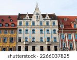 Facade of an ancient architectural buildings with white, red and yellow walls, tall windows, decorative elements and red roofs. Historical architecture. Old town. Poland, Wroclaw, January 2023.