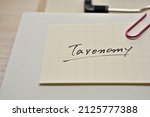 Small photo of A piece of paper clipped to the edge of the notebook has Taxonomy.