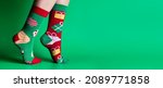 Small photo of Feet of obscured child in Christmas socks walking on tiptoes against green background