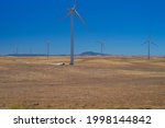 Small photo of Windustry, an airfoil lays on the ground afoot of a wind turbine on the wind farm.
