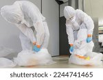 Small photo of Operators in type 5-6 hazmat suits performing decontamination procedure, after asbestos incident, careful take off of protective suit in a disposal big bag