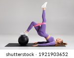 Fitness woman doing glute bridge exercise with resistance band on gray background. Athletic girl working out