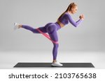Fitness woman doing exercise for glutes with resistance band on gray background. Athletic girl working out