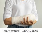 Close-up of a woman's broken arm in a cast. The girl holds a bent arm against the background of a white T-shirt. Appropriate treatment in Western medicine.