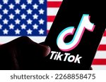 Small photo of TikTok app logo seen on smartphone screen. U.S. US flag o the blurred background. Stafford, UK, February 28, 2023