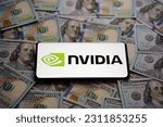 Small photo of Nvidia logo seen on smartphone which is placed on pile of US dollar bills. Concept. Selective focus. Stafford, United Kingdom, May 31, 2023