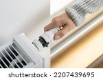 A woman in a warm sweater turns the regulator of the thermostatic radiator valve to the middle position to set the economical heating mode of the room. Heating of the apartment in the cold season.