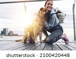 Happy Caucasian woman dressed in sportive clothing resting at boardwalk pier hugging and stroke lovely pet, fit girl with backpack smiling on leisure, concept of human love and friendship to dogs