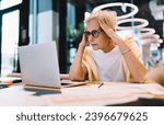 Small photo of Dumbfound senior woman sitting with laptop in modern workspace