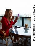 Small photo of Woman putting on her lip gloss looking at the mirror while sitting in the coffee shop, young businesswoman applying make up during her work break at cafe, elegant woman smarten up before a date