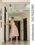 Small photo of ISLAMABAD, PAKISTAN - JANUARY 13, 2024 :Young beautiful classy girl standing on the floor in short frock dress in comfortable home interior