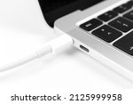 Charging battery laptop. Modern USB C port for fast charge. White cable plugged in laptop close-up view