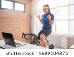Small photo of Asian woman cyclist. She is exercising in the house. By cycling on the trainer And playing online bike games, she is glad to succeed.