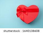 Red gift box heart-shaped on light blue table. Romantic background for Valentine Day or Birthday. Top view. Space for text. 