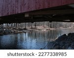 Small photo of Historic Frazier red wooden covered bridge over Little Muncy Creek in Lycoming County Pennsylvania built in 1888 against blue cloud sky. You can drive through it today. Built in the Burr Arch style.