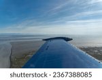 Small photo of Beechcraft Bonanza airplane wingtip flies over the Cook Inlet in Alaska. Fire Island wind farm powers Anchorage. Kenai mountains in background. Small aircraft are only way to see many areas of Alaska.