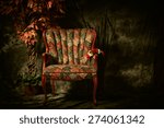 An empty, antique patterned chair shot in a chiaroscuro lighting style sitting next to artificial plant.