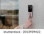 woman's hand uses a doorbell on the wall of the house with a surveillance camera