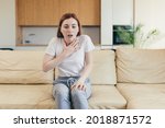 Young woman alone at home with a panic attack shortness of breath, trembling, numbness, loss of consciousness. Front view of a female suffering an anxiety sitting on a couch. chest pain, fear symptom
