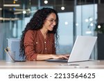 Small photo of Young and happy hispanic woman working in modern office using laptop, business woman smiling and happy in glasses and curly hair