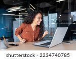 Small photo of Hispanic business woman celebrating victory success, employee with curly hair inside office reading good news, using laptop at work inside office holding hand up and happy triumph gesture.