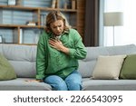 Small photo of Senior beautiful woman sitting sick on sofa at home. Holds his chest. He has asthma, allergies, feels severe pain, tenderness, panic attack, infarct.