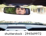 Small photo of Closeup portrait, angry young driver making stupid faces in rearview mirror reflection and sticking out tongue. Infuriated road rage concept, isolated interior car windshield background