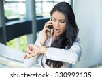 Closeup portrait, young woman in gray business suit blazer talking on cell phone concerned about running out of time on watch, isolated indoors office background