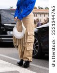 Small photo of Milan, Italy - September, 21, 2022: woman in blue denim asymmetric cropped jacket, leather bag with nailed studded fringed chain pendant shoulder, beige cargo flared pants, platform high heels shoes.