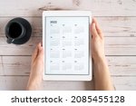 tablet computer with an open app of calendar for 2022 year and cup of tea or coffee in womans hands on wooden background. concept business or to do list goals with technology using. top view, flat lay