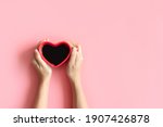 Flat lay of heart shaped cup of black coffee in the hands of women on pastel pink background with copy space. top view. Valentine's day, beverage and lifestyle concept