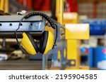 Small photo of Yellow protective ear muffs hang on machines in heavy industrial plants. The concept is a PPE device that protects against loud noise in the operator's environment. industrial work safety equipment
