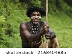 Small photo of Potrait of Dani tribe man from Wamena Papua Indonesia wearing traditional clothes for hunting is smiling against blurred greenery forest background.