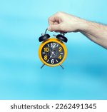 Small photo of Time concept. Alarm clock in a man's hand on a blue background on the clock hands 7 in the morning. Studio shot with a retro clock with an alarm clock.