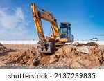 A powerful caterpillar excavator digs the ground against the blue sky. Earthworks with heavy equipment at the construction site